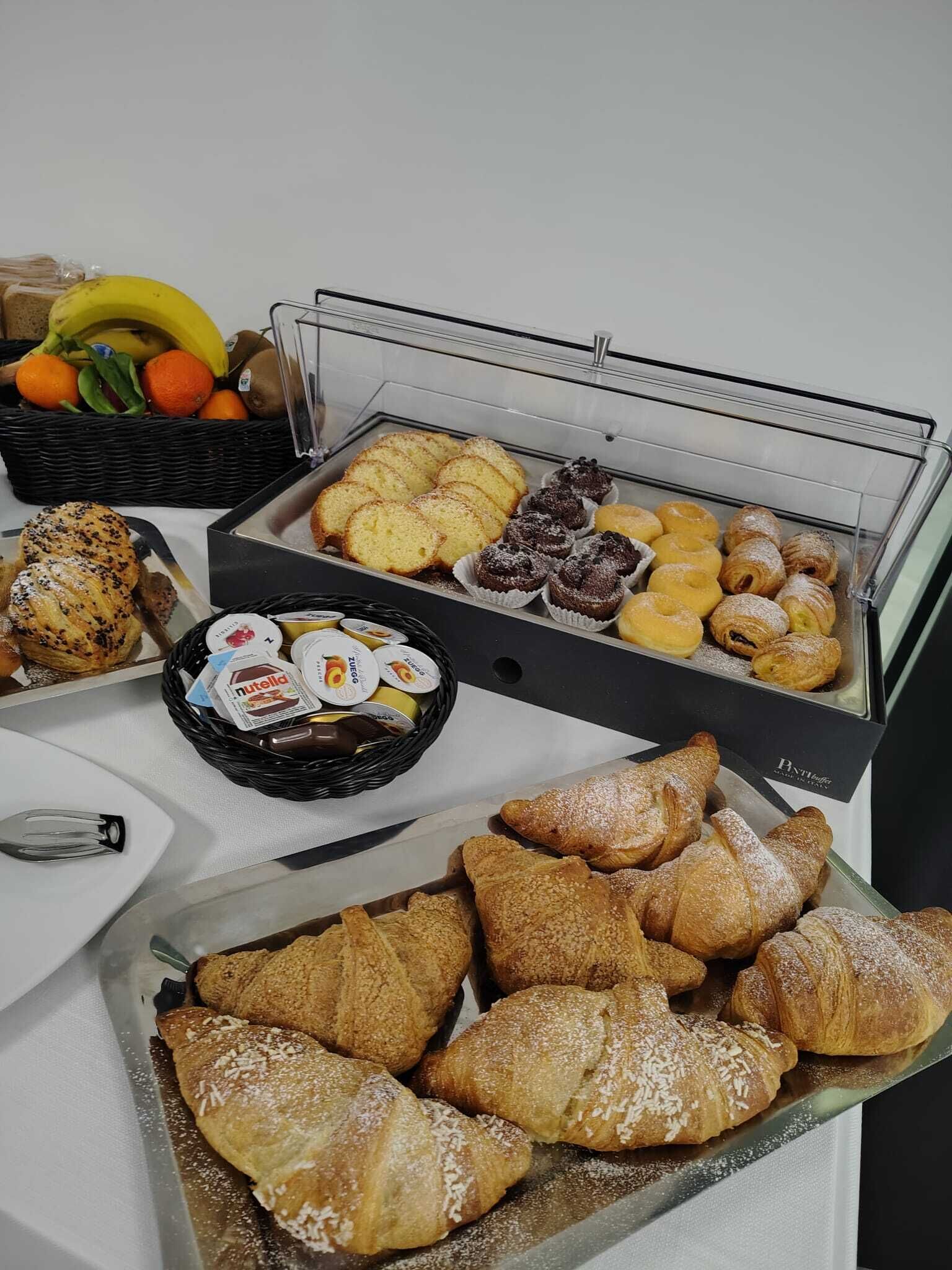 A buffet with various pastries, including croissants and muffins, and a basket of fruits.