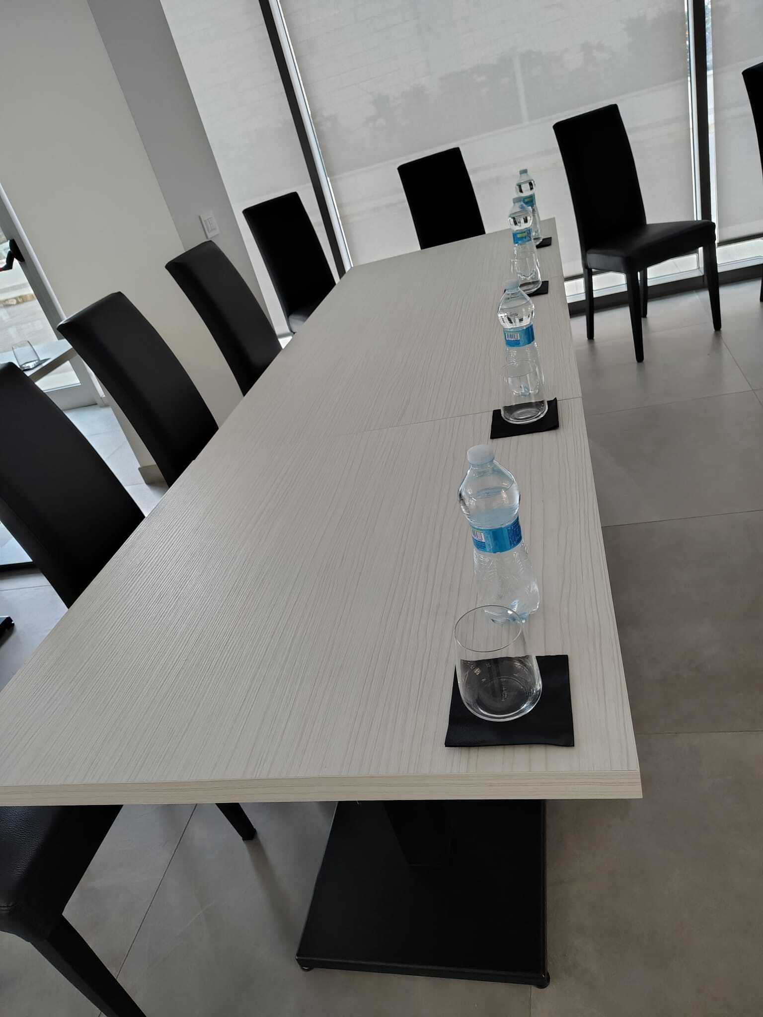 Un salón de conferencias con una larga mesa, sillas negras, botellas de agua y vasos.