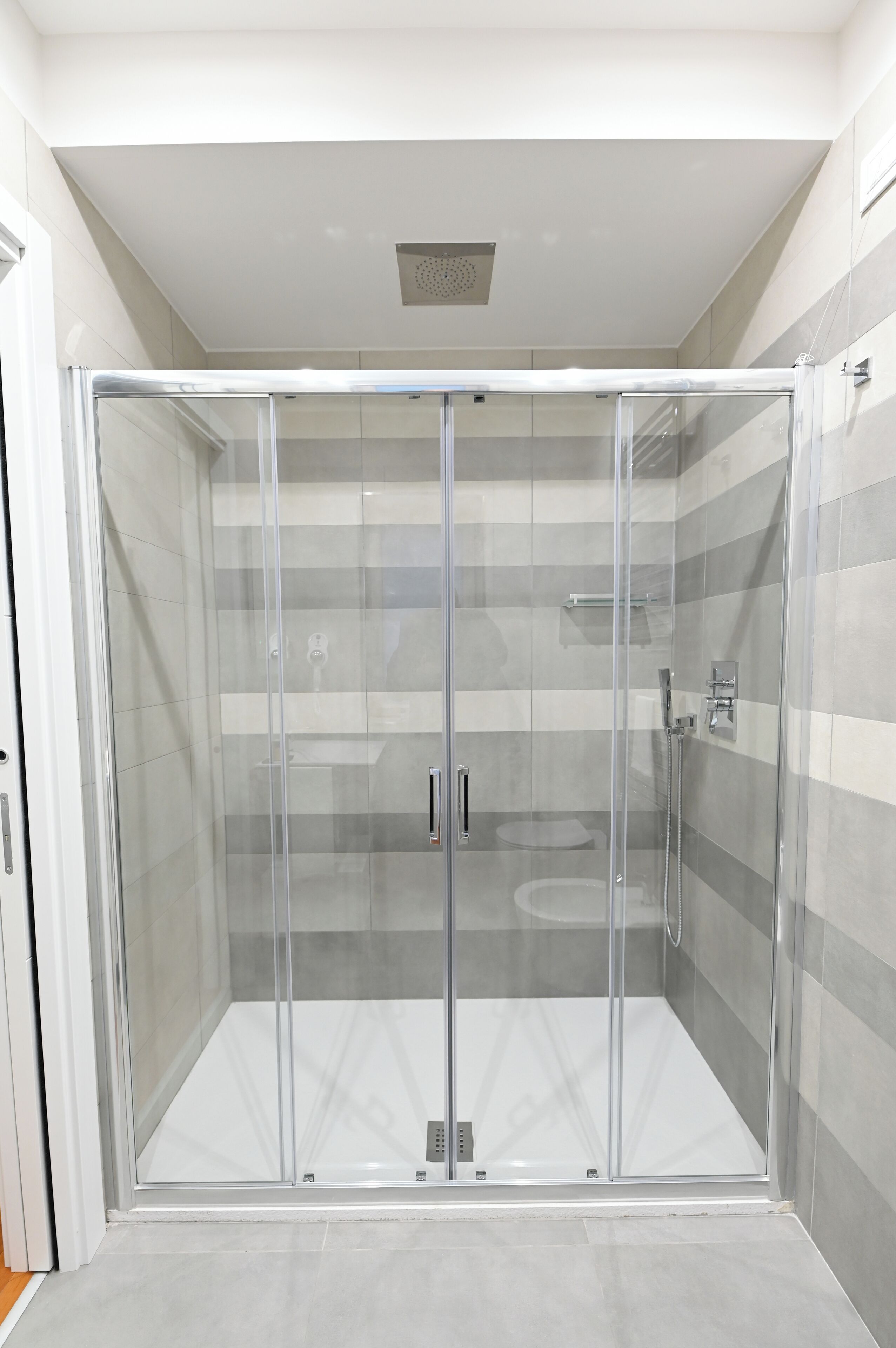 A glass-enclosed shower with a tiled floor and a ceiling vent.