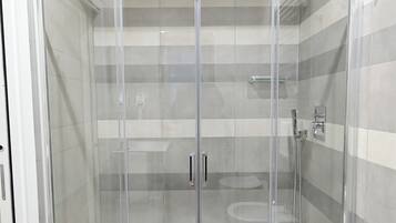 A glass-enclosed shower with a tiled floor and a ceiling vent.