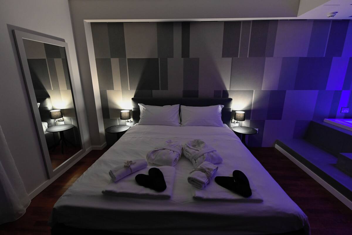 Hotelkamer met een groot bed, twee nachtkastjes met lampen, een spiegel en een muur met een geometrisch patroon.