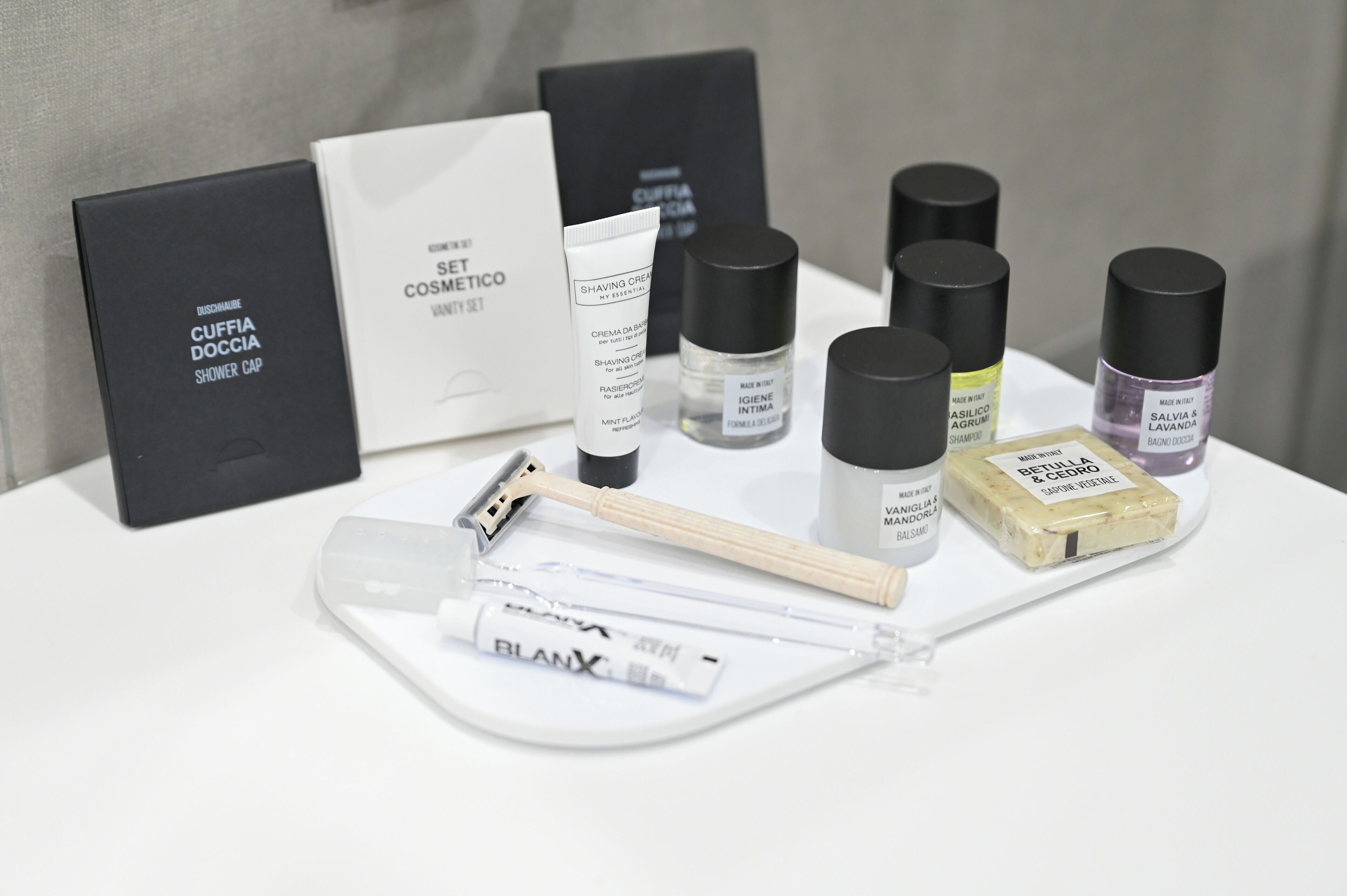 Une variété de produits de soins personnels, notamment un tube de crème à raser, un blaireau et un ensemble de produits de toilette, présentés sur un plateau blanc.