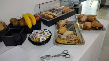 Une table de buffet proposant divers aliments, notamment des pâtisseries, des fruits et des en-cas emballés.
