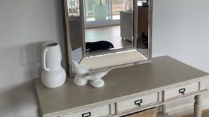 A white vanity with a mirror, a white electric kettle, and a decorative bird sculpture.