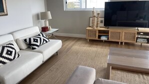 A modern living room with a white sofa, a coffee table, and a TV on a wooden stand.