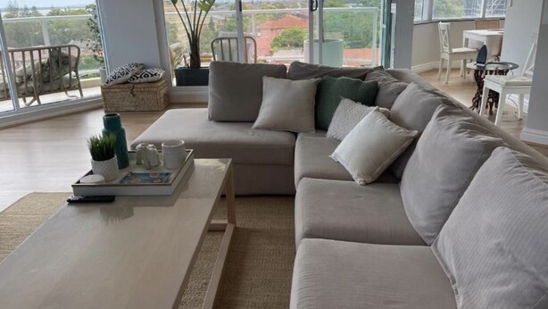 A modern living room with a beige sectional sofa, a coffee table, and a view of the outdoors through large windows.