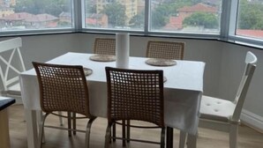 A dining area with a table and chairs, large windows with a view of buildings, and a woven light fixture.