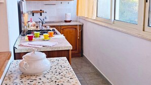 A small kitchen with wooden cabinets, a tiled backsplash, a countertop with a mosaic tablecloth, and a window with curtains.