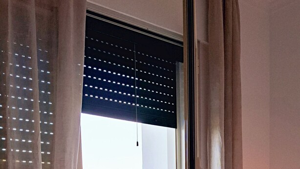 A hotel room with a bed, a balcony with wicker furniture, and a view of a yellow field.