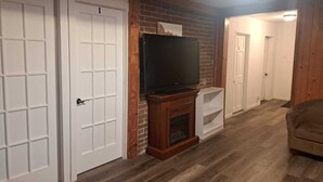 A hallway with a brick wall, a fireplace, and a television. - 4-BEDROOM APARTMENT FOR ALL-INCLUSIVE WORKERS | 5 MN PONT LAVIOLETTE  (Trois-Rivières)