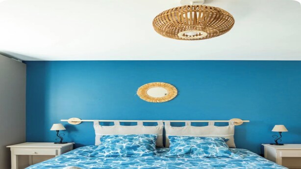 A bedroom with a blue wall, a bed with a blue floral bedspread, two pillows, a round mirror, and two bedside tables with lamps. - Atypical gîte Les Epinettes, 10 minutes from the beach in the Baie de Somme  (Cayeux-sur-Mer)