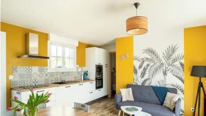 A modern kitchen with white cabinets, a wooden countertop, and a tiled backsplash. There is a dining table with chairs, a sofa, and a small side table. - Atypical gîte Les Epinettes, 10 minutes from the beach in the Baie de Somme  (Cayeux-sur-Mer)