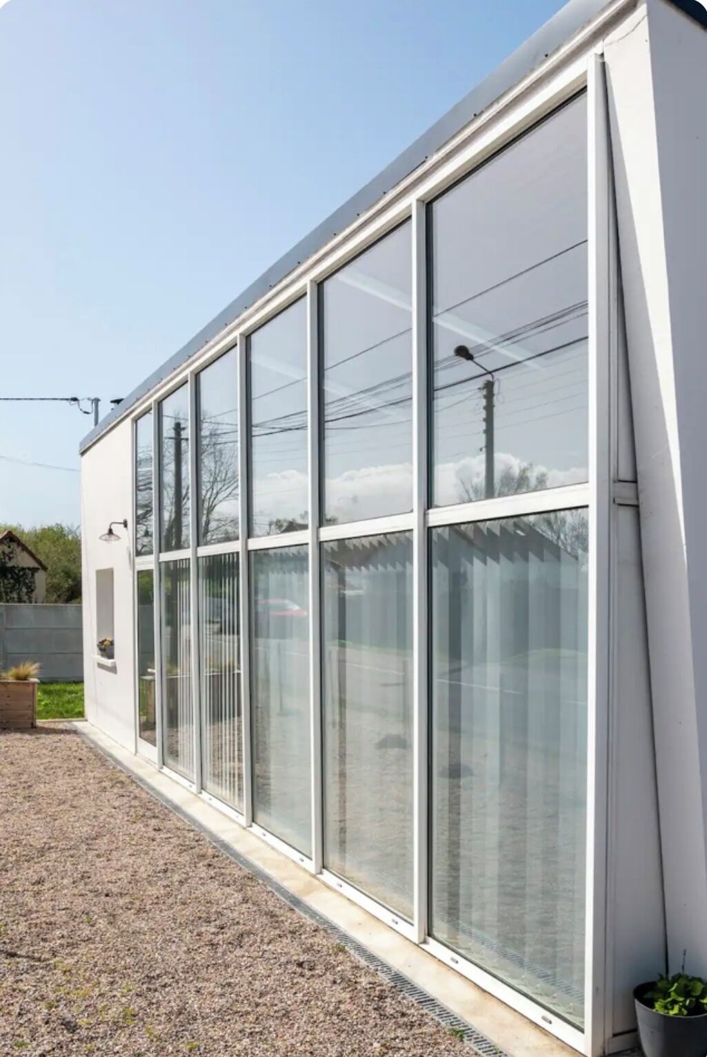 A modern building with large glass windows, a gravel driveway, and a small garden area.