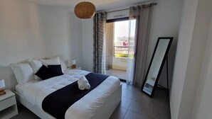 A hotel room with a large bed, a bedside table with a lamp, a mirror, and a view of the outside.