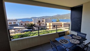 A balcony with a table and chairs, overlooking a coastal area with buildings and a view of the sea.
