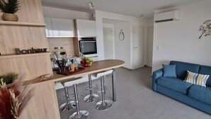 A modern kitchen with white cabinets, a wooden countertop, and a bar area with stools. There is a blue sofa with a decorative pillow in the living area.