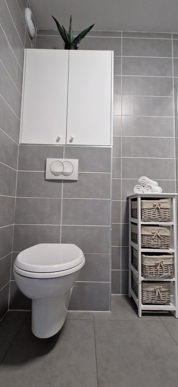 A bathroom with a toilet, a white cabinet, and a shelf with baskets.