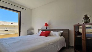 Ein Hotelzimmer mit Bett, Nachttisch, Lampe, Schrank und Blick auf ein Gebäude durch ein Fenster.
