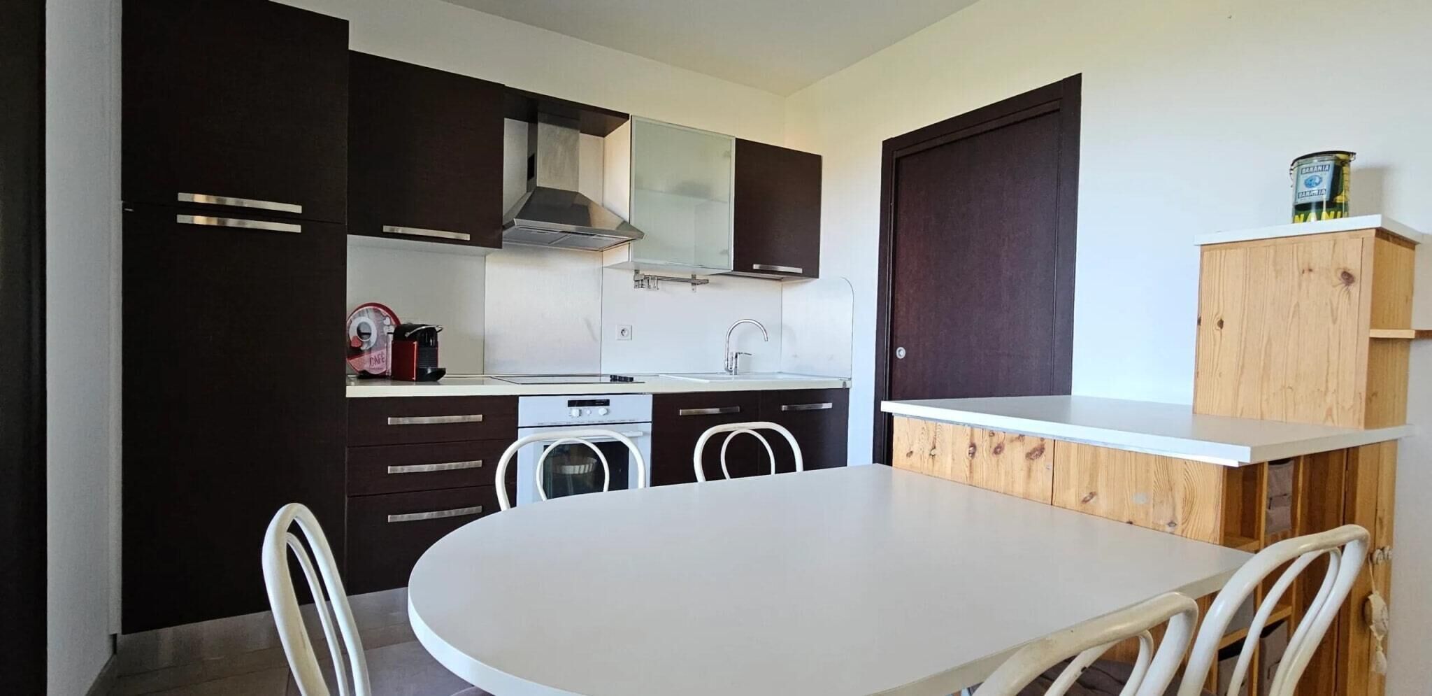 A compact kitchen with dark cabinetry, a white countertop, and a round dining table with chairs.