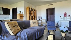 Ein Wohnzimmer mit einer Couch, zwei Sesseln, einem Couchtisch, einem Bücherregal, einer Uhr und einem kleinen Tisch mit Blumen.