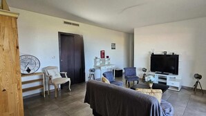 Ein Wohnzimmer mit einer Couch, Sesseln, einem Fernseher, einem kleinen Tisch und einem Bücherregal.