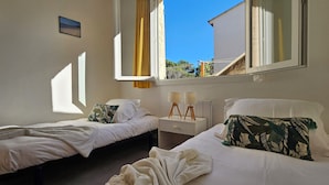 A bedroom with two beds, a nightstand with a lamp, and a window with a view of the outside. - T3 Paradise on the beach, feet in the water (Olmeto)