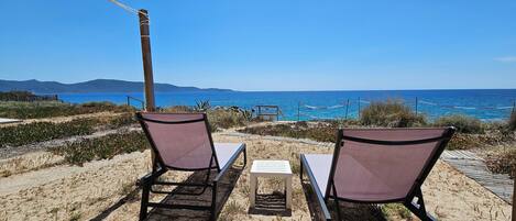 Two beach chairs facing the sea with a wooden deck and a rope barrier.