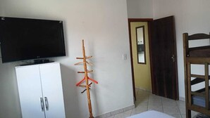 Un dormitorio con cama, armario, televisor montado en la pared y una silla de madera.