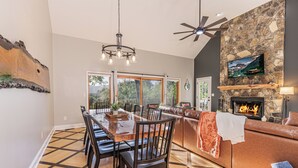 A spacious living area with a fireplace, a dining table with chairs, and a large window offering a view of the outdoors. - Mountain Views, Game Room, Firepit and Hot Tub in Bryson City (Bryson City)