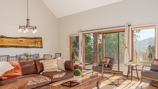 A spacious living room with a brown leather sofa, a wooden coffee table, and a large window offering a view of the outdoors. - Mountain Views, Game Room, Firepit and Hot Tub in Bryson City (Bryson City)