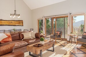Un salon spacieux avec un canapé en cuir marron, une table basse en bois et une grande fenêtre donnant sur l’extérieur.