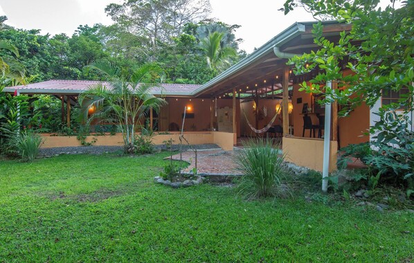 A two-story building with a covered patio area, surrounded by lush greenery and a well-maintained garden.