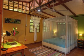 A bedroom with a bed under a canopy, a desk with a laptop, a chair, a plant, and a painting on the wall.