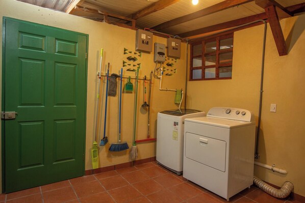 A laundry room with a green door, a washing machine, and various cleaning tools.