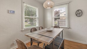 A dining area with a wooden table, six chairs, and a hanging light fixture. - ModernNest-KS Bed| Fire Pit• Near TU•Expo•Downtown (Tulsa)