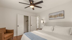 A bedroom with a bed, a ceiling fan, a brown chair, and a painting on the wall. - ModernNest-KS Bed| Fire Pit• Near TU•Expo•Downtown (Tulsa)