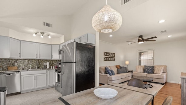 A modern kitchen with white cabinets, a stainless steel refrigerator, and a dining area with a wooden table and chairs. - ModernNest-KS Bed| Fire Pit• Near TU•Expo•Downtown (Tulsa)