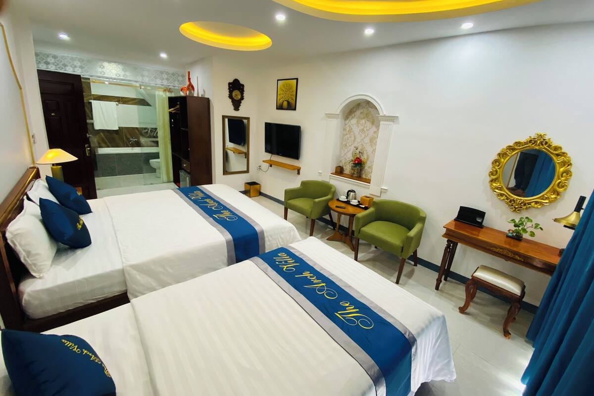 A hotel room with two beds, a desk, a chair, a TV, and a bathroom visible through an open door.