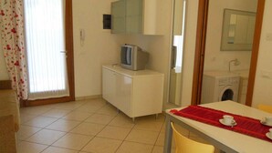A compact hotel room with a kitchenette, a television, a washing machine, and a dining area with a table and chairs. - Holiday apartment with air conditioning and garden (Bibione)