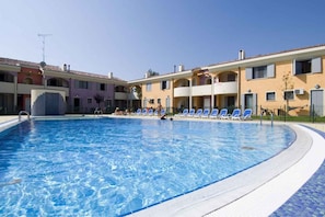 A swimming pool with lounge chairs, a building with balconies, and a clear sky.