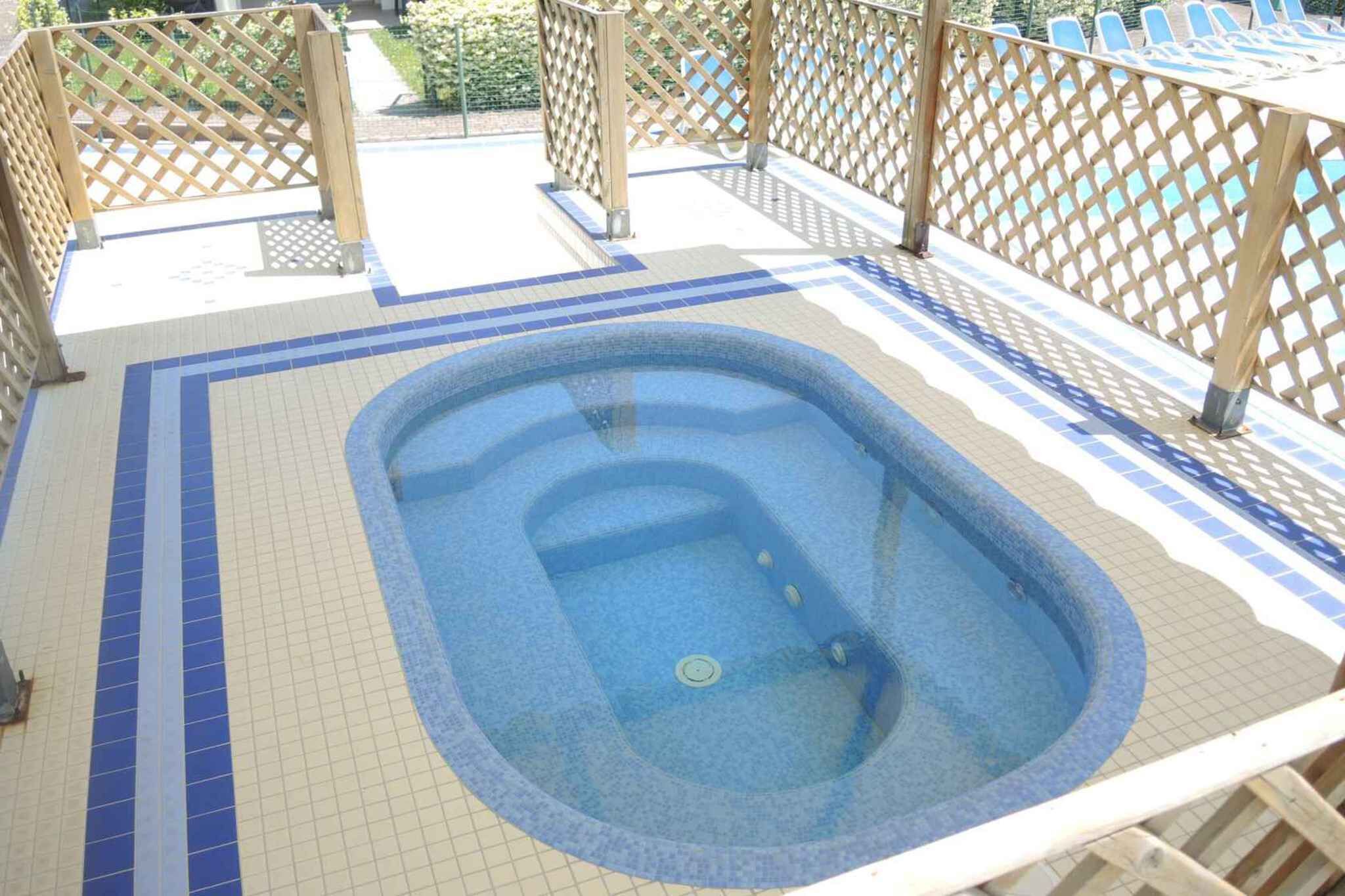 Un bain à remous doté d’une terrasse carrelée, entouré d’une clôture en bois.