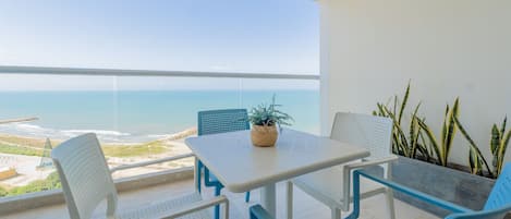 Un balcone con tavolo bianco e sedie blu, vista sulla spiaggia e sull'oceano.
