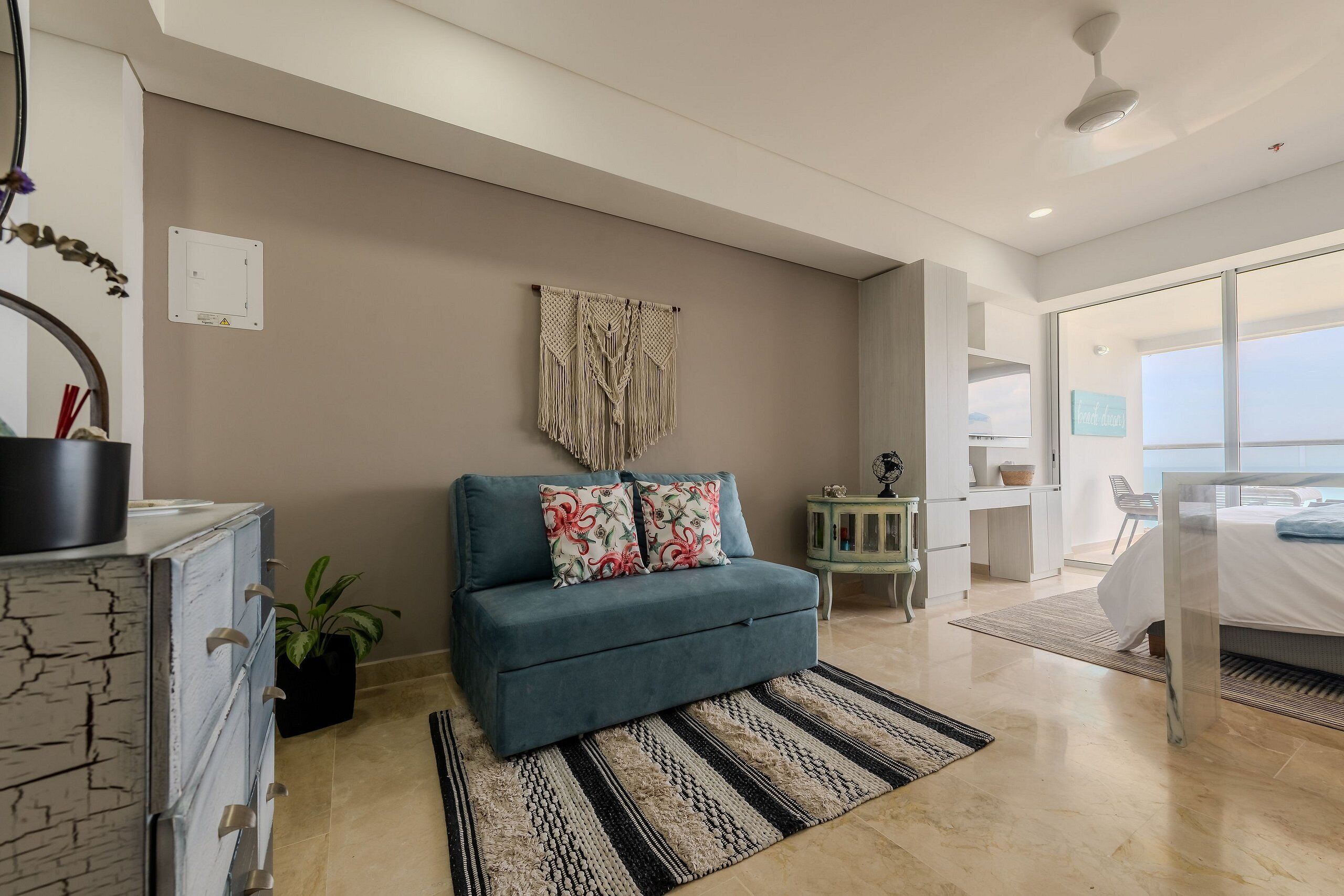 A modern living room with a sofa, a patterned rug, and a wall-mounted macrame piece.