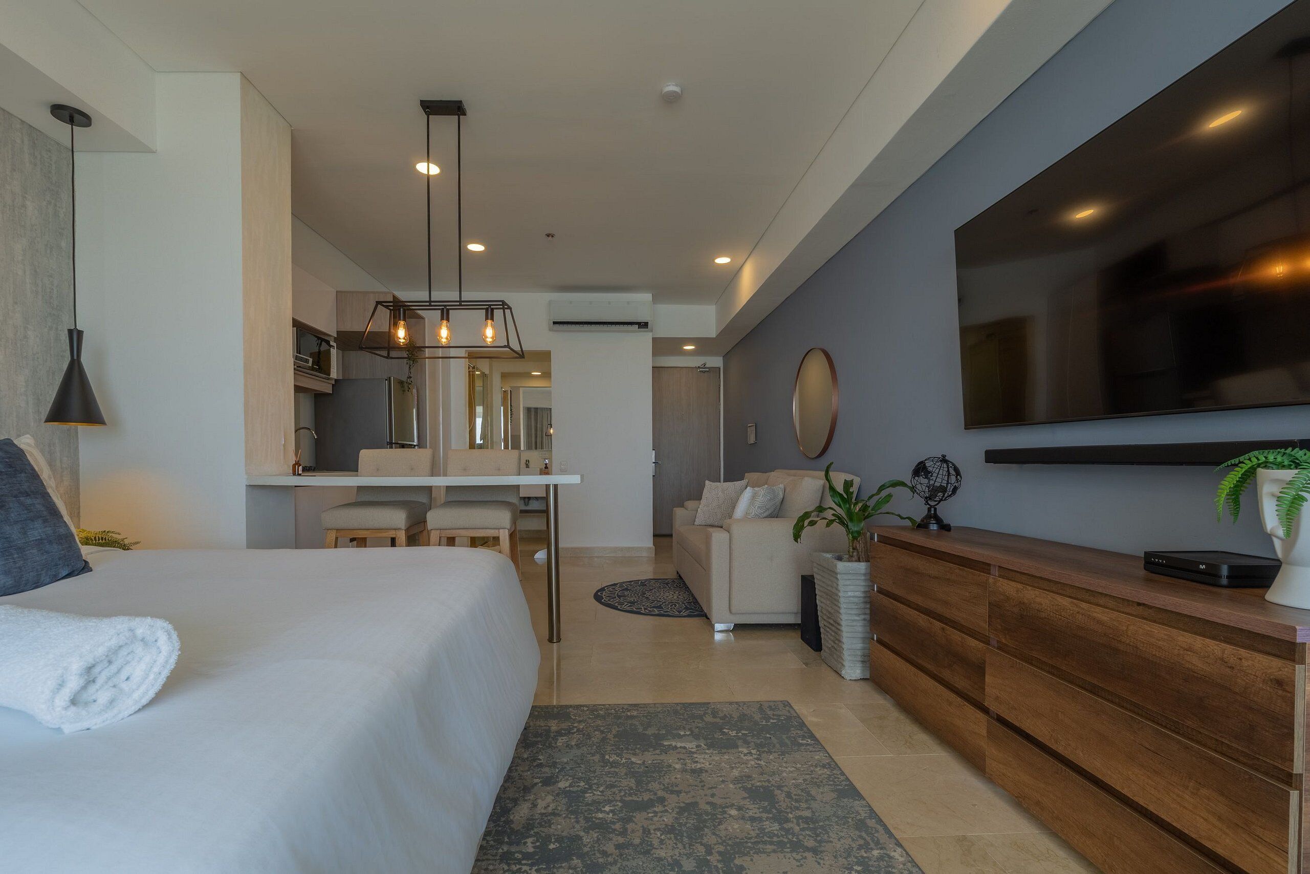 A modern hotel room with a large bed, a dining area, a sofa, a TV, and a wooden cabinet.