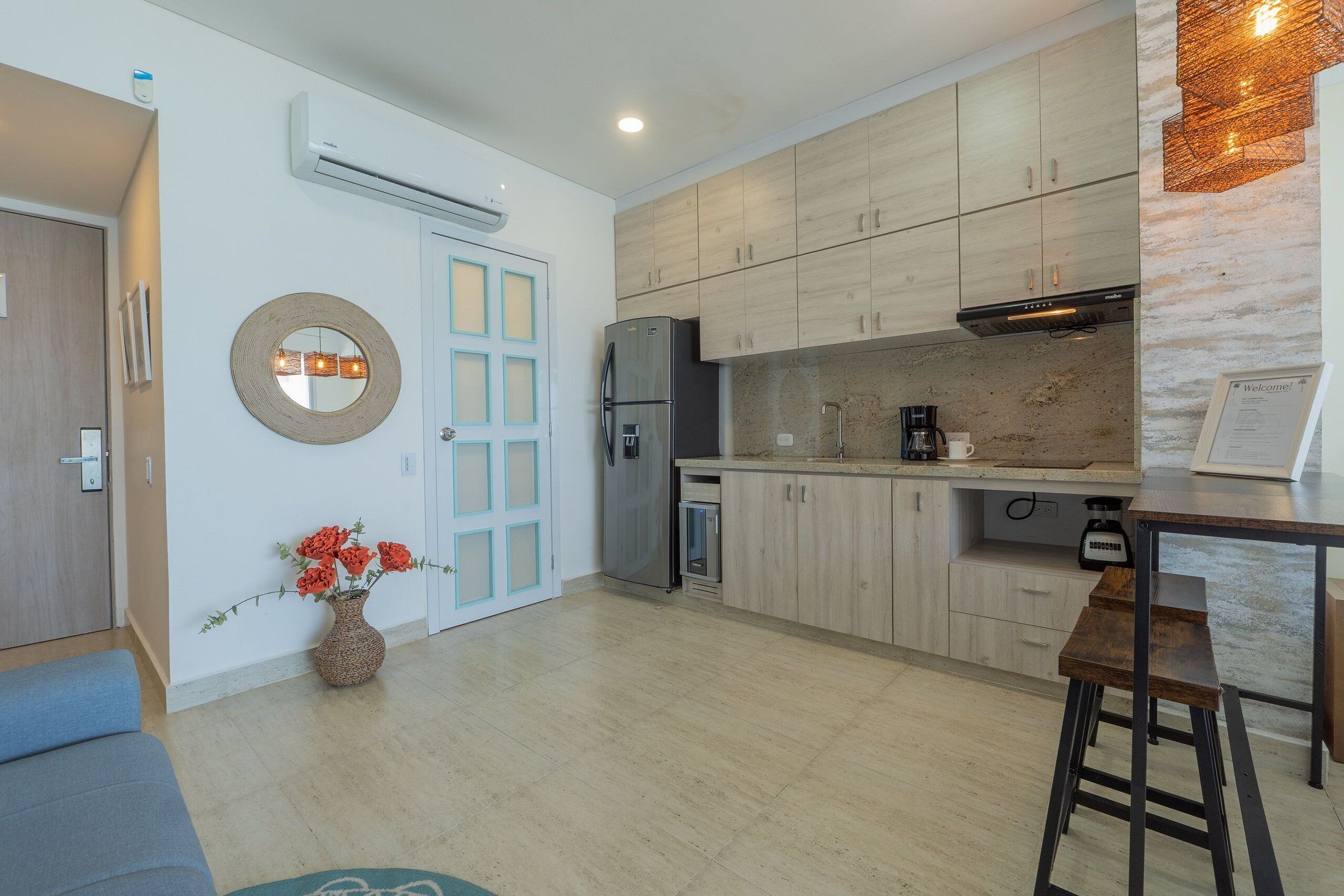A modern kitchen with light wood cabinets, a stainless steel refrigerator, and a coffee maker.