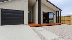 A modern house with a garage, a wooden deck, and a large sliding glass door leading to an interior space.