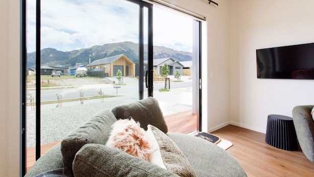 A modern living room with a large sliding glass door leading to a view of a residential area with houses and mountains.