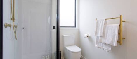 A bathroom with a glass-enclosed shower, a toilet, a window, and a towel rack with towels.