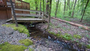 Eine Holzterrasse mit einer Brücke über einen Bach in einem bewaldeten Gebiet.