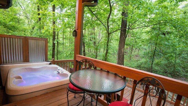 Eine Holzterrasse mit Whirlpool, Glastisch und roten Sitzgelegenheiten.